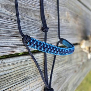 May include: A black and blue braided rope halter for horses. The halter is made of two different colors of rope, black and blue, and is braided together to create a unique design.