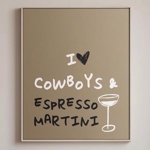 Op de afbeelding: Een ingelijste poster met de tekst "I ❤️ Cowboys & Espresso Martini" in een eetkamer. De poster is bruin met witte tekst en een zwart hart. De kamer heeft een tafel, stoelen en een vaas met takken.