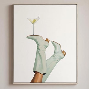 May include: A framed art print depicts a martini glass balanced on the heel of a light green boot. The artwork is set in a dining room with a marble table, wooden chairs, and a tall vase with branches.