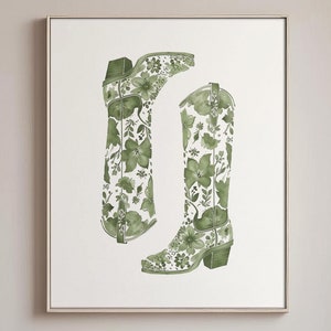 Op de afbeelding: Een ingelijste print met een aquarel illustratie van twee groene cowboylaarzen met een bloemmotief. Het kunstwerk wordt tentoongesteld in een eetkamer met een tafel, stoelen en een decoratieve vaas.