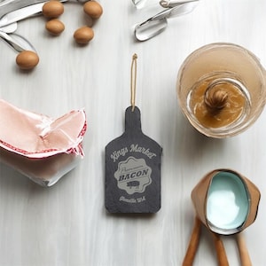 May include: A black slate sign with a rope hanger. The sign reads "Kings Market Premium Bacon,  Glenville WA". A pig is pictured in the center of the sign.