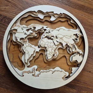 Könnte beinhalten: Eine mehrschichtige Weltkarte aus Holz, die Kontinente und Länder zeigt. Die Karte ist kreisförmig, mit hellen und dunklen Holztönen, die einen 3D-Effekt erzeugen. Die Kontinente sind aufwendig ausgeschnitten und geschichtet, mit einer hellen Holzfarbe.
