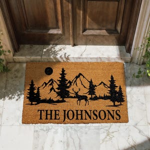 A mat with a mountain landscape and a deer silhouette, with the text "THE JOHNSONS" printed on it.