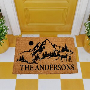 A yellow door with a mat featuring a mountain landscape and a deer, with the text "THE ANDERS" printed on it.