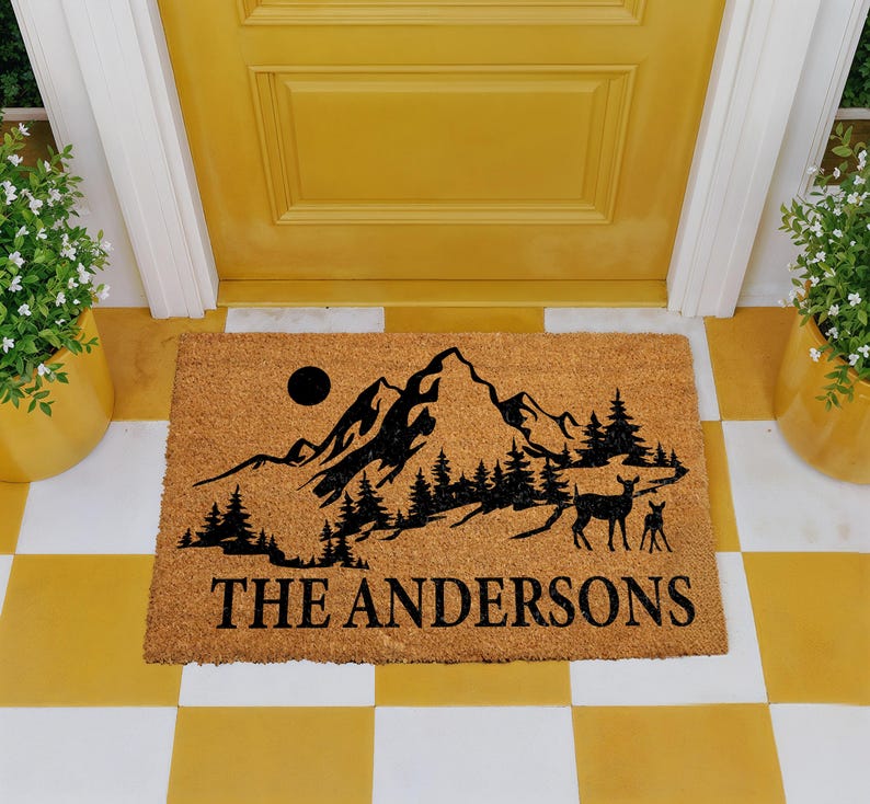 A yellow door with a mat featuring a mountain landscape and a deer, with the text "THE ANDERS" printed on it.