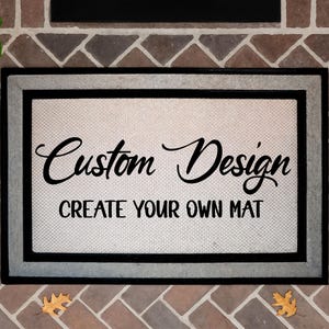 May include: Rectangular doormat with a light beige center and a black border. The mat features the words "Custom Design" in a cursive font above "CREATE YOUR OWN MAT" in a sans-serif font.