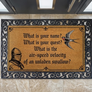 May include: A rectangular tan coir doormat with a black decorative scrollwork border. The mat features a black illustration of a knight in a helmet and a flying swallow, with the text: What is your name? What is your quest? What is the air-speed velocity of an unladen swallow?