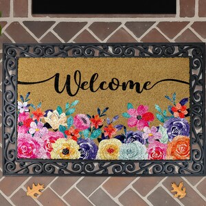 A decorative welcome mat with a floral design and the word "Welcome" written on it, placed on a brick wall.