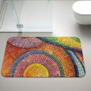 May include: A rectangular bath mat with a colorful mosaic design. The mat features a vibrant array of colors, including red, orange, yellow, green, and blue, arranged in a semi-circular pattern. The mat is placed on a light gray floor in a bathroom setting.