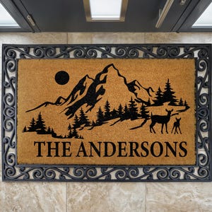 a door mat with a mountain landscape and a deer silhouette, along with the name "The Andersons" written on it.