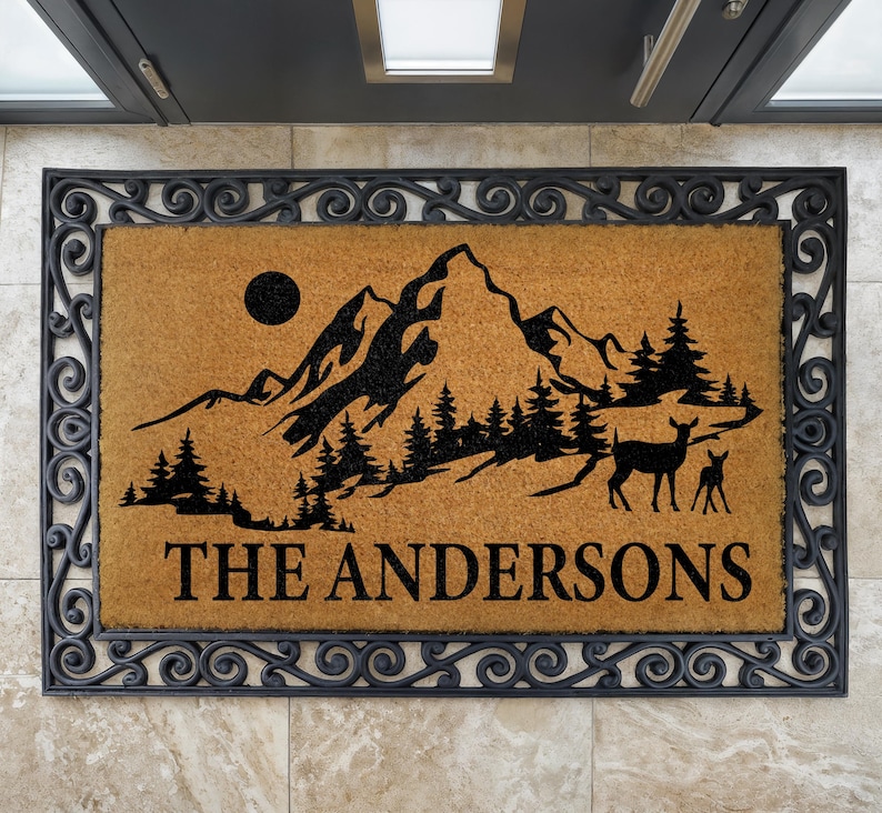 a door mat with a mountain landscape and a deer silhouette, along with the name "The Andersons" written on it.