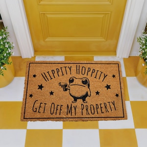 A yellow door with a black and white checkered floor, and a rectangular door mat with a cartoon frog holding a gun and the text "Hippity Hopped My Property" printed on it.