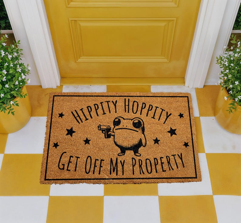A yellow door with a black and white checkered floor, and a rectangular door mat with a cartoon frog holding a gun and the text "Hippity Hopped My Property" printed on it.
