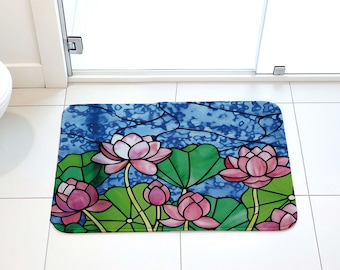 May include: A rectangular bath mat featuring a stained glass style design of pink lotus flowers and green lily pads against a textured blue background. The pattern is composed of distinct segments outlined in dark lines.