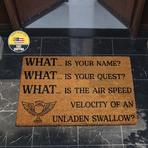 May include: A rectangular doormat made of natural fibers. The mat features black text that reads "WHAT... IS YOUR NAME?" and other questions. A winged goblet graphic is also present. The mat is placed on a tiled floor.