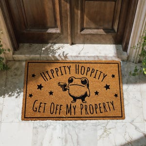 A door mat with a cartoon frog holding a gun and the text "Hippity Hopperity Get off my property" printed on it.