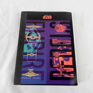 May include: A black notebook with a Star Wars theme. The cover features various starships and the words "STAR WARS" in red and the word "EMPIRE" in purple and teal.
