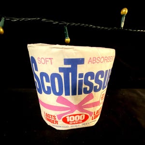 May include: A white cardboard tube of ScotTissue bathroom tissue with a pink ribbon and the text "Soft Absorbent ScotTissue Lasts Longer 1000 Sheets Bathroom Tissues 12.5 SQ. FT. ONE PLY 444"