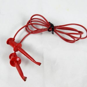 May include: Red test leads with alligator clips. The leads are connected to a bundle of red wire, secured with a black cable tie. The alligator clips are designed to connect to electrical components for testing purposes.