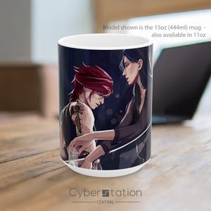 May include: A white ceramic mug featuring a dark-toned illustration of two characters, one with red hair and mechanical arm markings, the other with long dark hair. The text on the mug reads: Model shown is the 15oz (444ml) mug - also available in 11oz.
