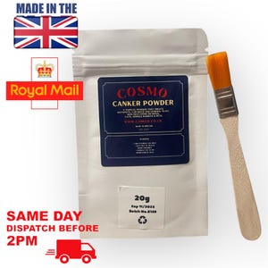 May include: A white pouch with a blue label that reads "COSMO CANKER POWDER" and a smaller label that reads "20g Exp 11/2023 Batch No. 8139". A small orange brush with a wooden handle is next to the pouch.