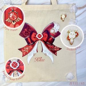 Puede incluir: Un bolso tote beige de lona con un gran diseño de lazo rojo, detalles blancos y el nombre "Klee". También presenta un emblema "Pyro Vision", un "Dodoco Pin" y una ilustración "Klee's Clover Emblem".