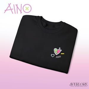 Può includere: T-shirt girocollo nera con un piccolo disegno ricamato raffigurante un cuore, una chiave e la parola "AINO". La parola "AINO" è scritta anche in un carattere stilizzato sopra la maglietta. La maglietta è un merchandising fatto dai fan.