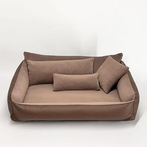 May include: A rectangular pet bed in shades of brown, featuring a textured outer rim and a smooth interior base. The bed includes three matching brown cushions: one long rectangular bolster, one smaller rectangular pillow, and one square pillow.
