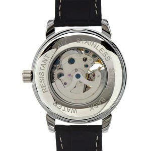 May include: A silver-toned, water-resistant watch with a black leather band. The watch's back is transparent, showcasing the intricate mechanical movement. The words "All Stainless Steel" and "Water Resistant" are visible.