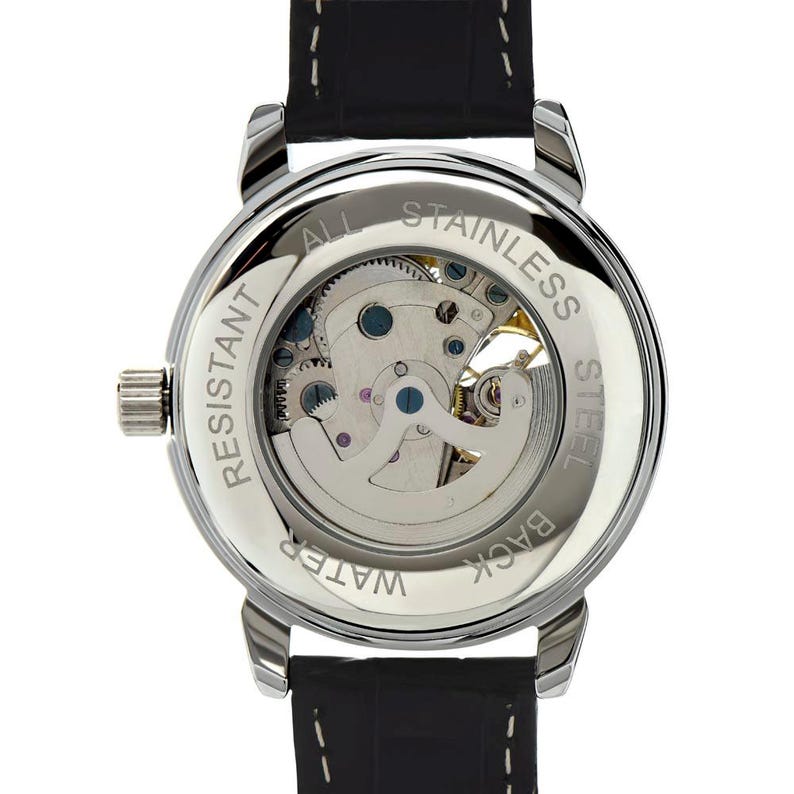 May include: A silver-toned, water-resistant watch with a black leather band. The watch's back is transparent, showcasing the intricate mechanical movement. The words "All Stainless Steel" and "Water Resistant" are visible.