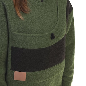 May include: Green fleece pullover with a high collar and a black zip. The pullover has a black horizontal stripe across the chest and a small brown rectangular patch near the bottom. The fabric has a textured, nubby appearance.