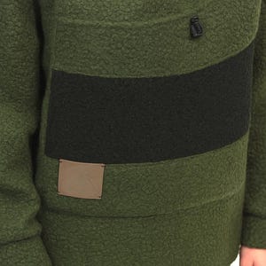 May include: Green fleece pullover with a black stripe across the chest. The pullover features a half-zip and a small, square patch on the lower front. The fabric has a textured, fuzzy appearance. Part of a clothing collection.