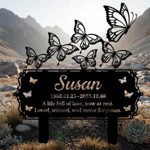 Pu&ograve; includere: Paletto commemorativo da giardino in metallo nero con il nome "Susan", date e un'iscrizione. Il design include ritagli di farfalle. Lo sfondo mostra una catena montuosa.