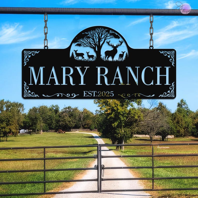 May include: Black metal sign with the text "MARY RANCH" and "EST.2025". The sign features a silhouette of deer and a tree. The sign is hanging from a metal bar with chains. The background shows a ranch entrance.