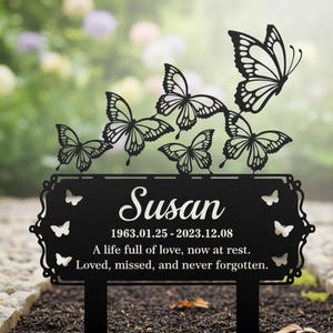 Pu&ograve; includere: Un paletto commemorativo da giardino in metallo nero con il nome "Susan" e le date 1963.01.25-2023.12.08. Il paletto ha un bordo decorativo e ritagli di farfalle, con il testo "A life full of love, now at rest. Loved, missed, and never forgotten."
