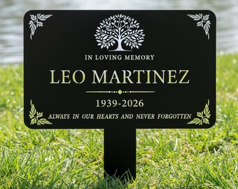 Può includere: Paletto da giardino commemorativo nero con la scritta "IN LOVING MEMORY LEO MARTINEZ 1939-2026 ALWAYS IN OUR HEARTS AND NEVER FORGOTTEN." Presenta una grafica ad albero e decorazioni angolari. Posizionato nell'erba verde vicino all'acqua.