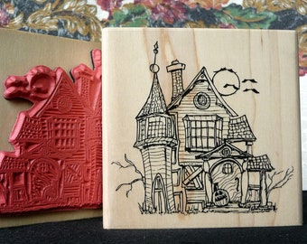 May include: Two wooden blocks with a spooky house design. One block has a red rubber stamp of a house with a detailed design. The other block has a black and white line drawing of a house with a tower and a moon in the background.