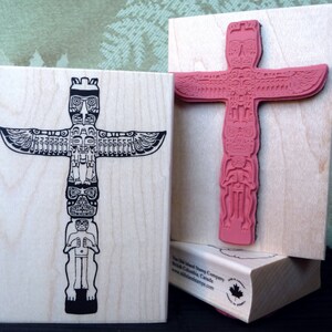 Puede incluir: Dos sellos de madera con un diseño de tótem. Un sello muestra una ilustración negra detallada del tótem, el otro es un sello de goma rosa del mismo diseño. Los sellos están sobre un bloque de madera de color claro.