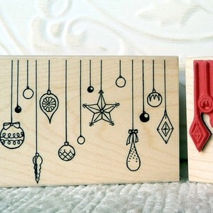 Puede incluir: Dos bloques de madera con diseños de adornos navideños. El bloque de la izquierda tiene adornos en blanco y negro colgando de cuerdas. El bloque de la derecha tiene adornos rojos colgando de cuerdas.