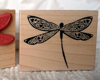 May include: Two wooden blocks with dragonfly stamps. The left block features a red dragonfly with intricate details. The right block features a black dragonfly with intricate details.