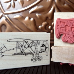 Puede incluir: Dos bloques de madera con un diseño de avión vintage. El bloque superior presenta un avión rojo con una hélice y el bloque inferior presenta un contorno en blanco y negro de un avión.