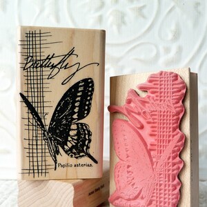 May include: Two wooden rubber stamps with butterfly designs. The first stamp features a black and white butterfly with the text "Butterfly" and "Papilio asterias." The second stamp features a pink butterfly with a patterned background.