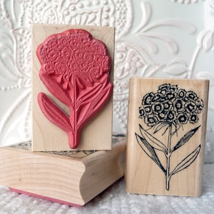 May include: Two wooden rubber stamps with floral designs. The first stamp features a red flower with a detailed design. The second stamp features a black and white flower with a simple design.