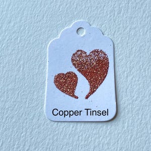 May include: A white gift tag with two copper glitter hearts and the text "Copper Tinsel".