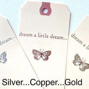 May include: Three gift tags with the text "dream a little dream..." printed on them. Each tag features a different colored butterfly: silver, copper, and gold.