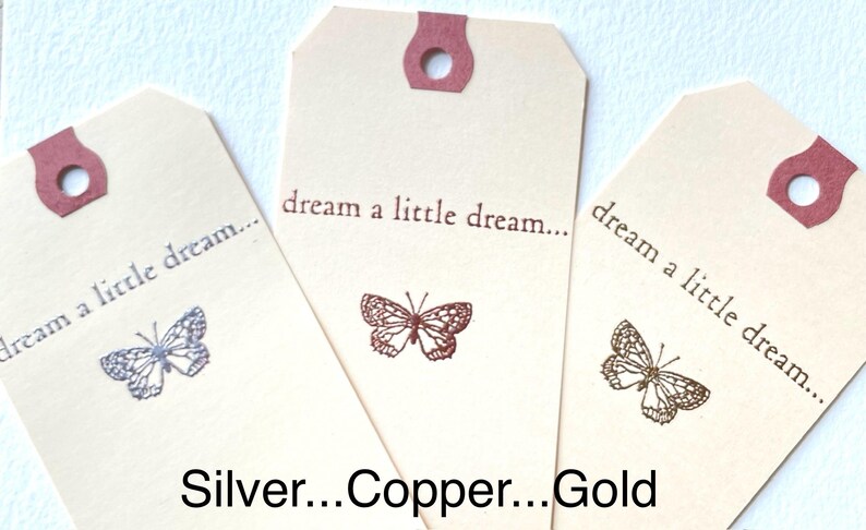 May include: Three gift tags with the text "dream a little dream..." printed on them. Each tag features a different colored butterfly: silver, copper, and gold.