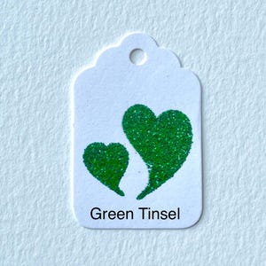 May include: A white gift tag with a green glitter heart design. The tag says "Green Tinsel" at the bottom.