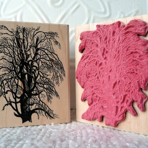 May include: Two wooden blocks with different designs carved into them. The block on the left has a black silhouette of a tree with branches. The block on the right has a pink design of a tree with branches.