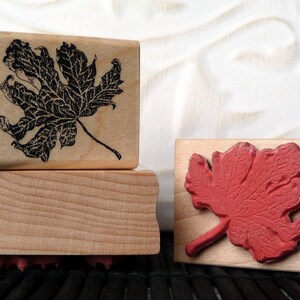 May include: Two wooden blocks with leaf designs. The top block has a black leaf design and the bottom block has a red leaf design.