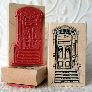 Puede incluir: Dos sellos de goma de madera con imágenes de puertas antiguas. El primer sello es rojo y presenta una puerta doble con un diseño decorativo. El segundo sello es en blanco y negro y presenta una puerta doble con una corona a cada lado y el número 157 sobre la puerta.